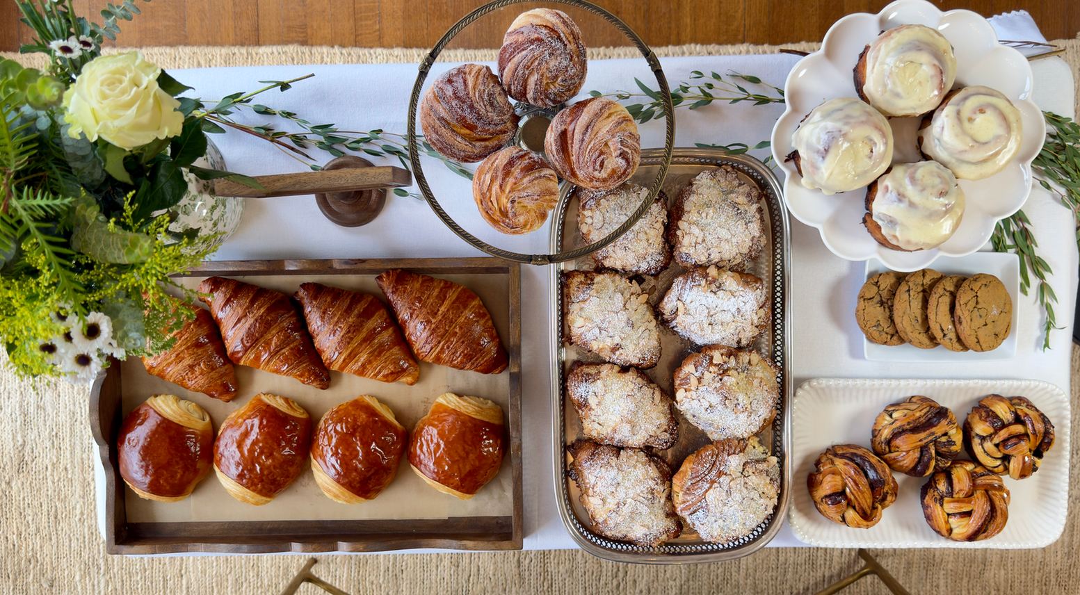 An overhead spread of pain au chocolat, almond croissants, cruffins, cinnamon rolls and cookies