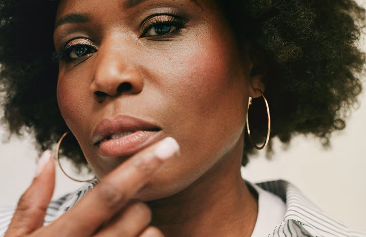 Close-up of a woman with hoop earrings touching her lip, wearing striped clothing.
