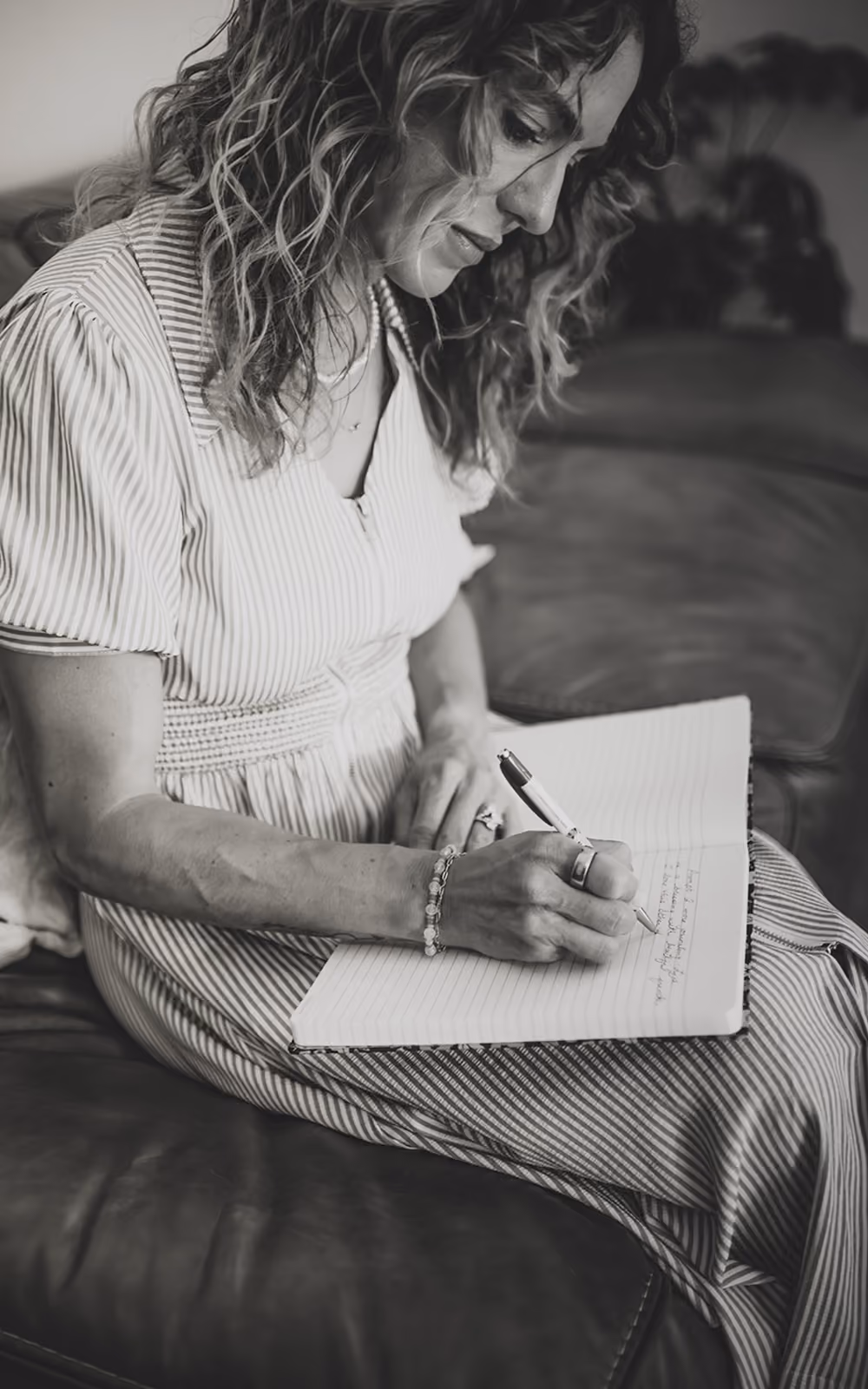 Kelly Hyde sitting on a couch writing in a lined notebook with a pen.