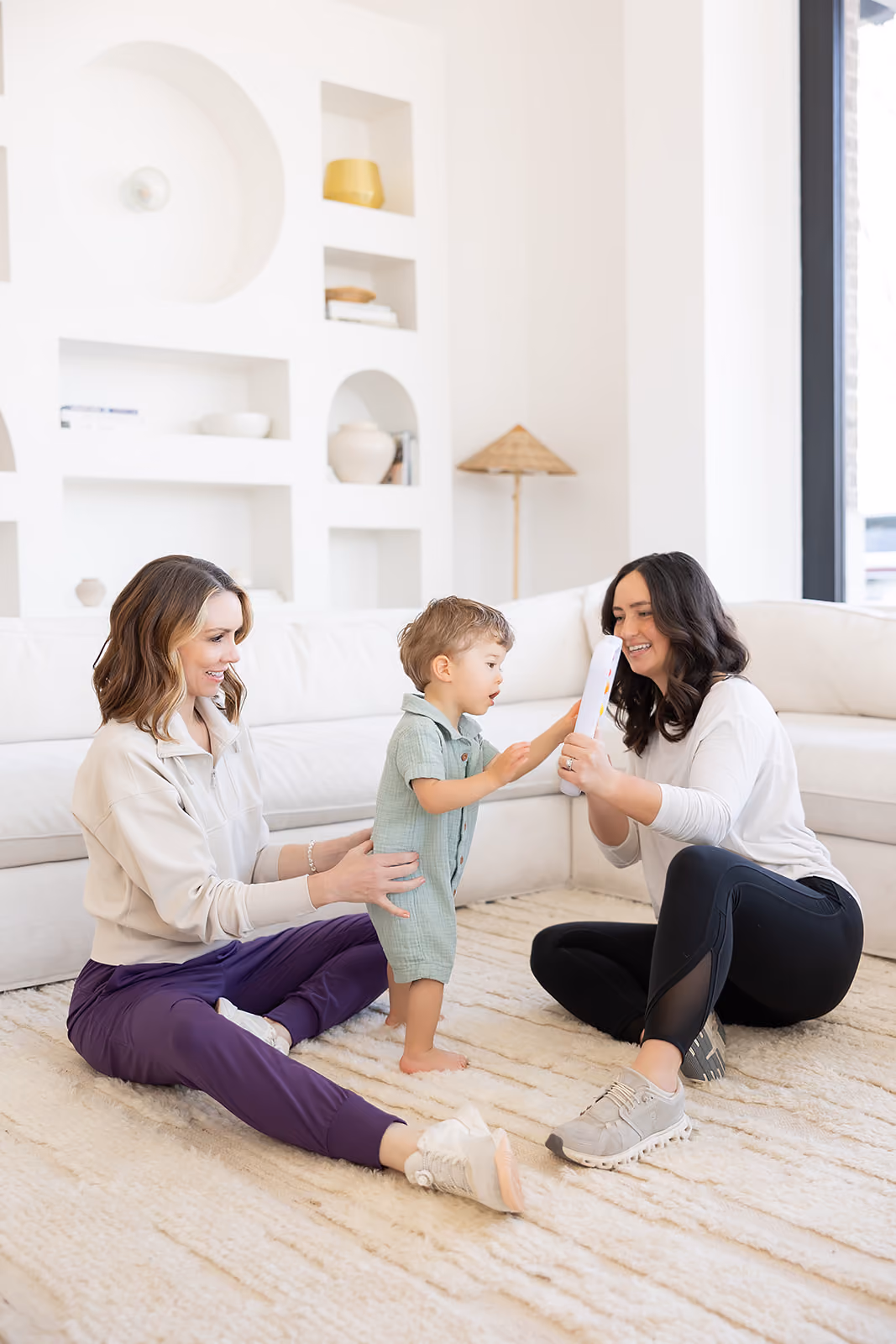 A physical therapist guiding a baby through a gross motor exercise on the floor