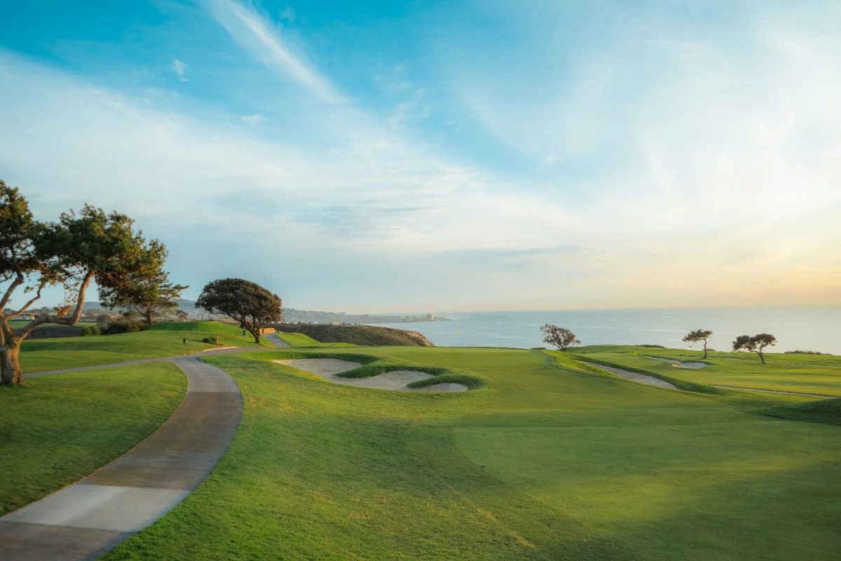 Golden-hour view of a coastal golf course, fairway curving along the cliffs above the ocean.