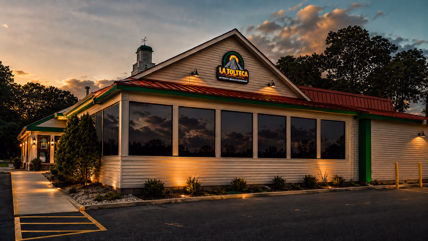 La Tolteca restaurant building at dusk with lit exterior and reflective windows showing cloudy sky.