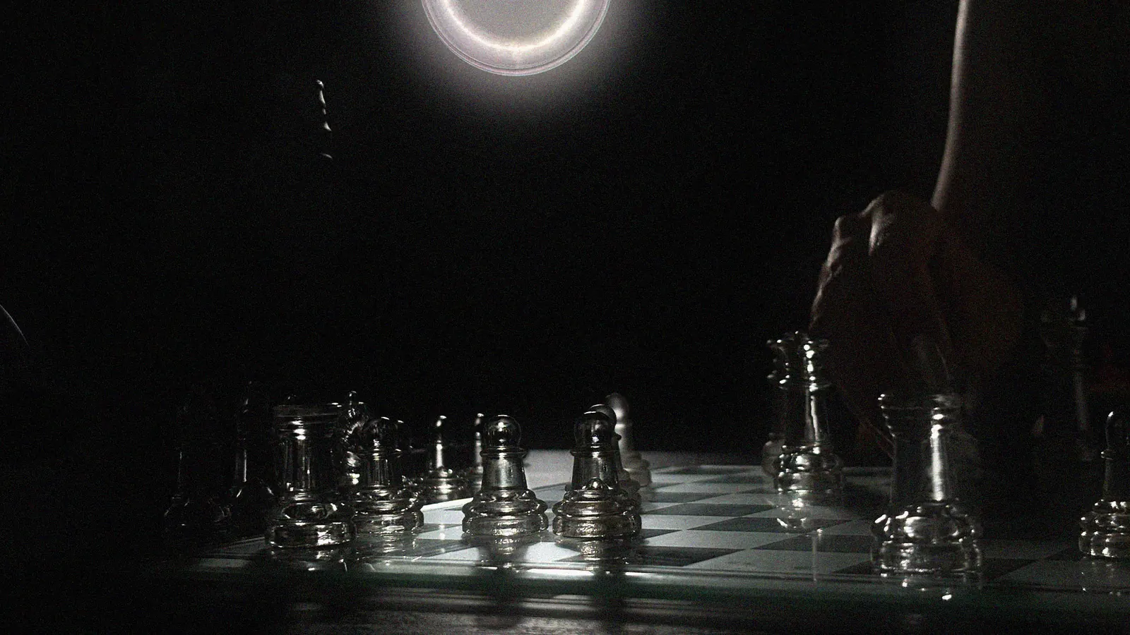 A glass chessboard under a ring light, a hand mid-move
