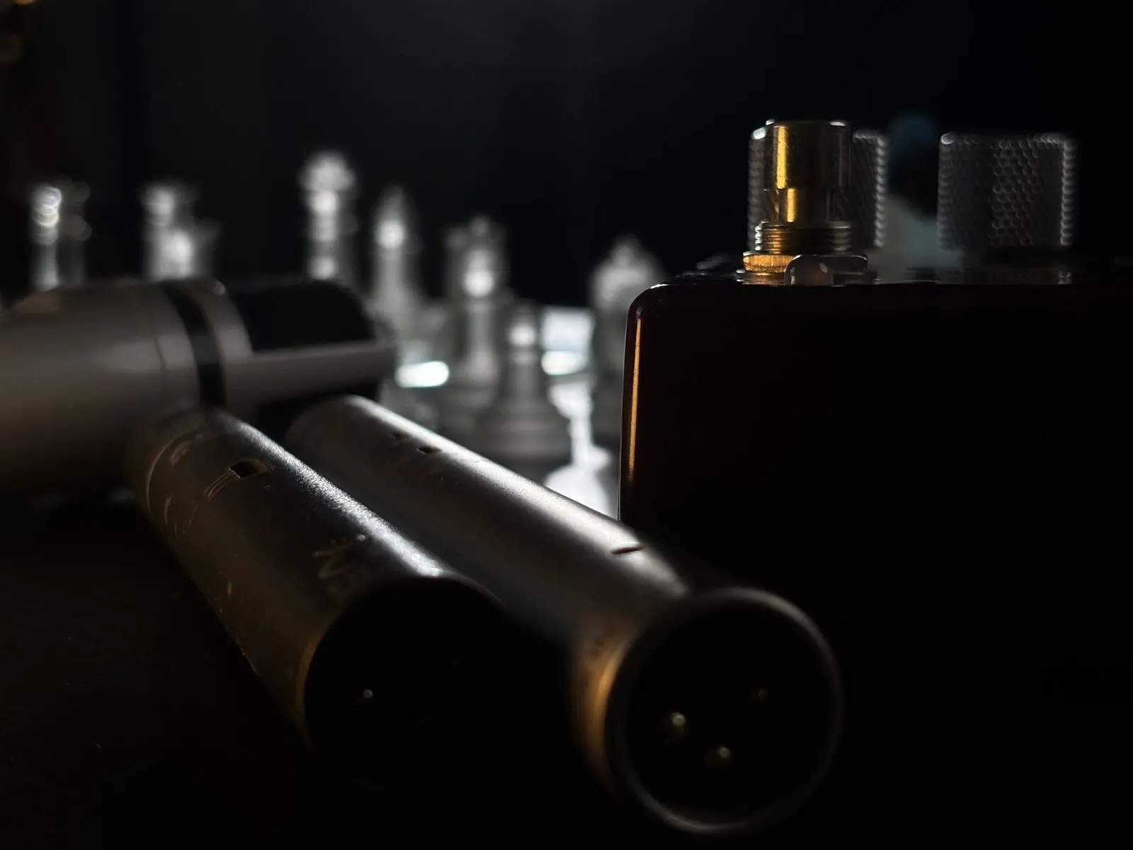 Two pencil condenser microphones on a desk, glass chess pieces behind