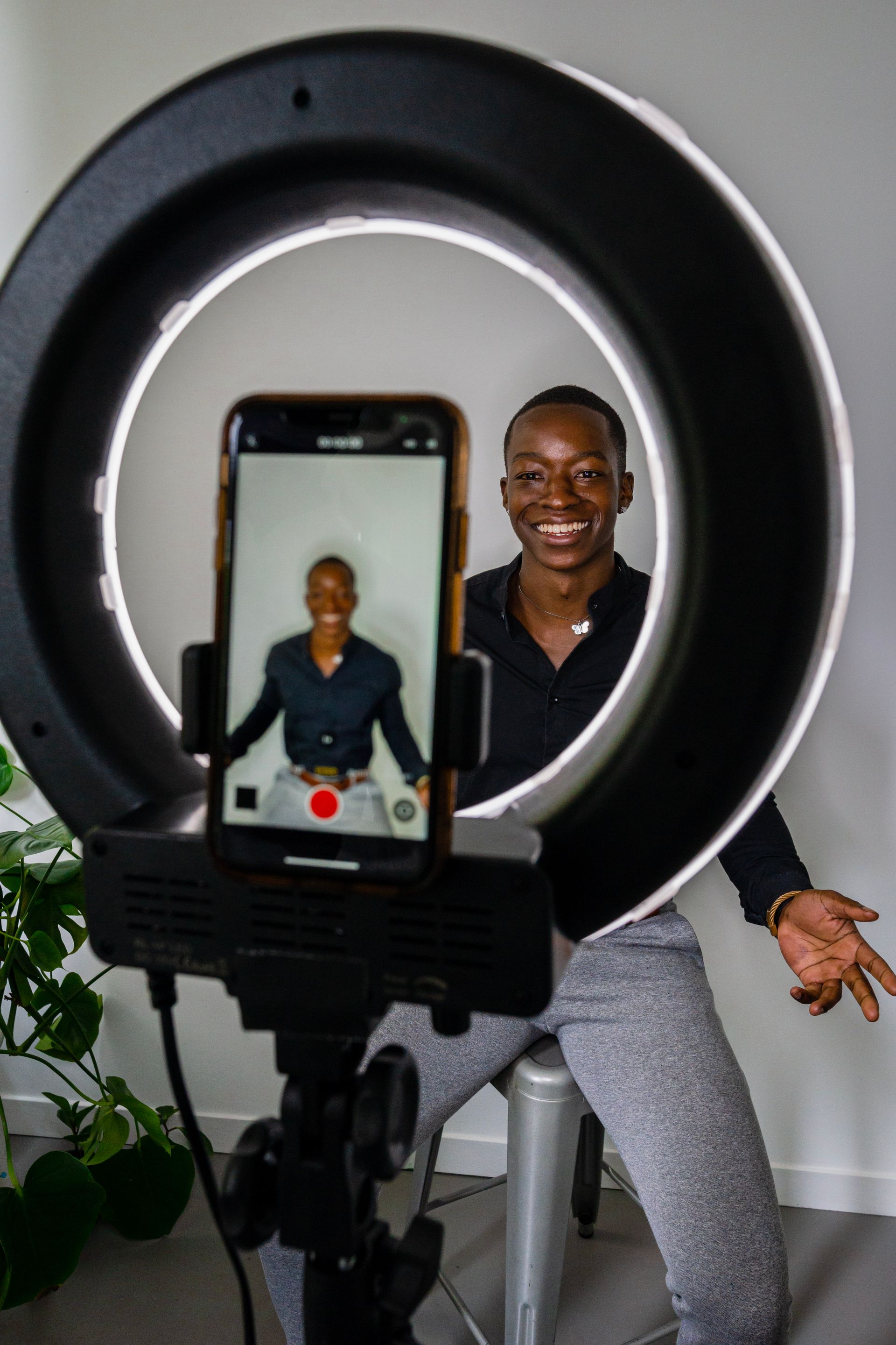 A smiling creator recording video with a smartphone and ring light