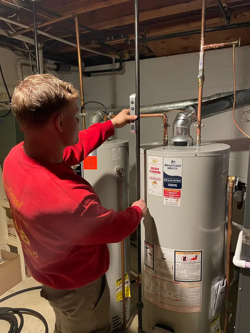 Man working on a water heater with plumbing tape, in a basement or utility area.