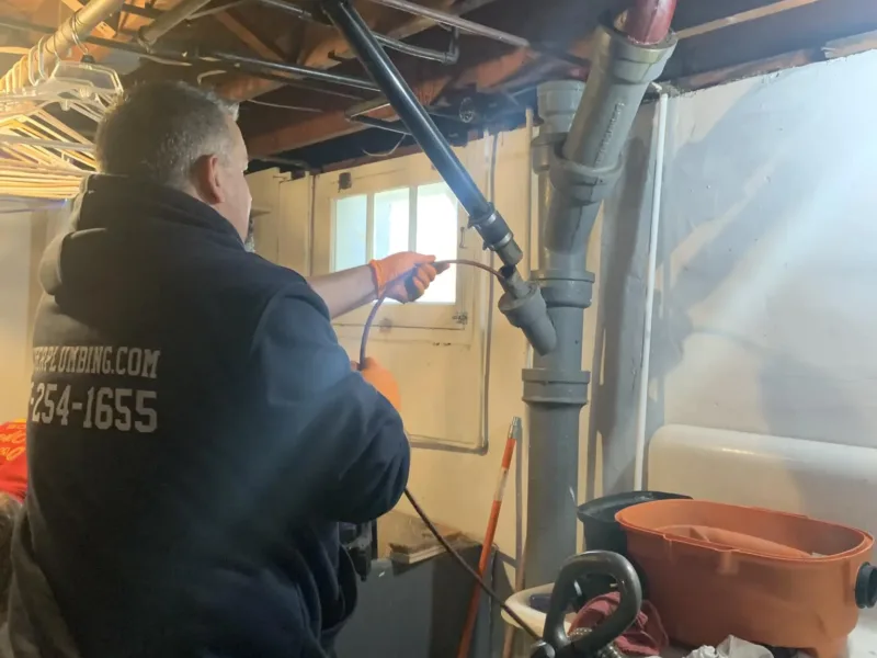Two plumbers in hoodies working on a sink, with phone numbers and website on their backs.