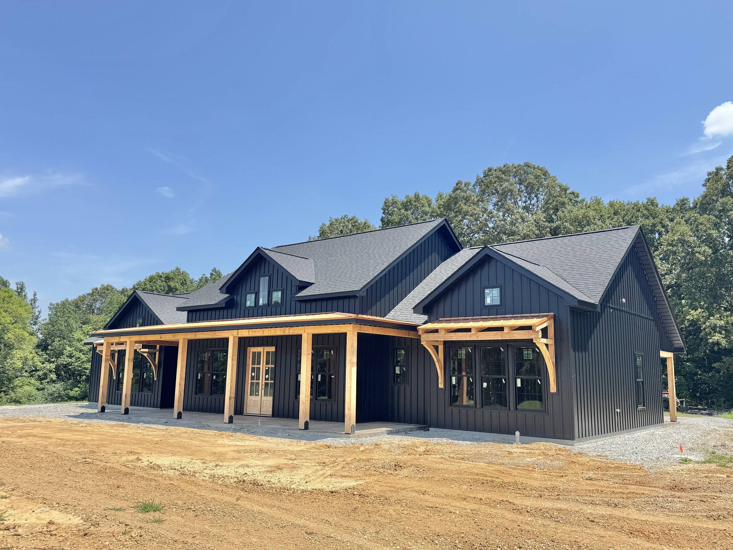 Custom black board-and-batten barndominium built by CM Construction with cedar timber-frame porch