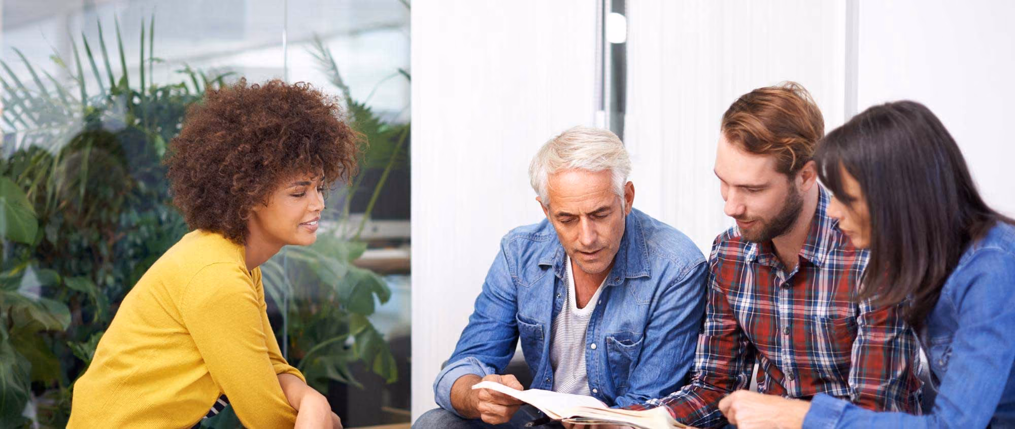 Four co-op board members in NYC sitting indoors in discussion, one man reading from a book while others listen attentively.