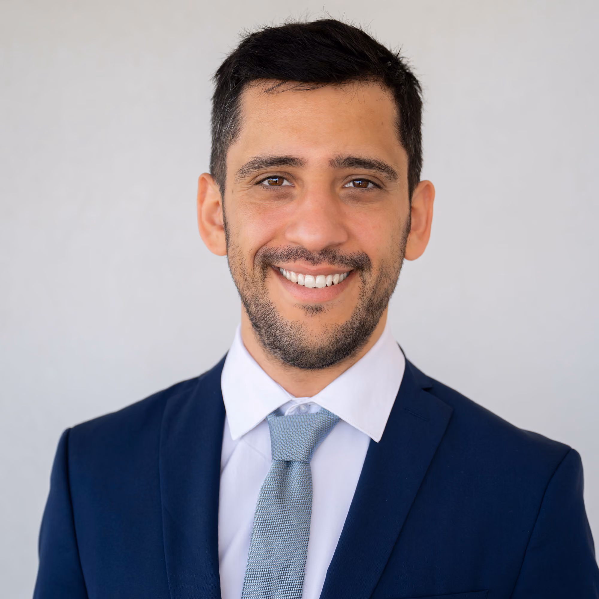 A smiling Ori Efroni, founder of NYC TaxAbate Advisors, with short dark hair wearing a white shirt, light blue tie, and dark blue suit jacket.
