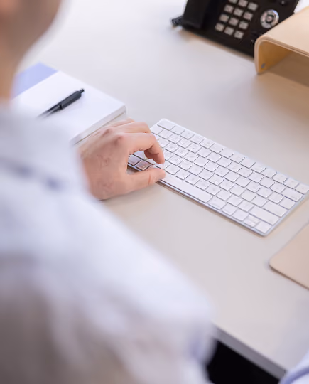 Close-up of a hand using a mouse on a minimalist desk setup with a white keyboard, conveying attention to detail and precision in a digital workspace.