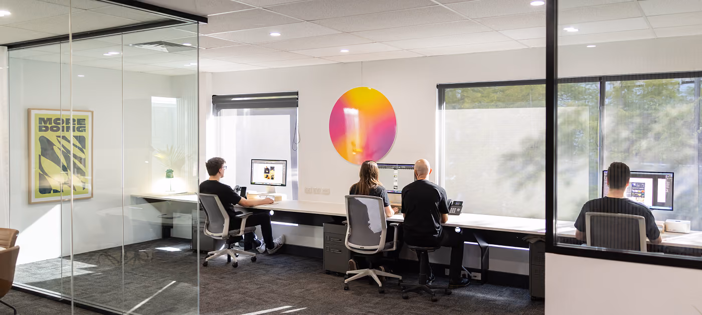 Team gathered in a roundtable discussion, sharing ideas in a bright and relaxed office space with plants and clean design—reflecting open communication and shared thinking.