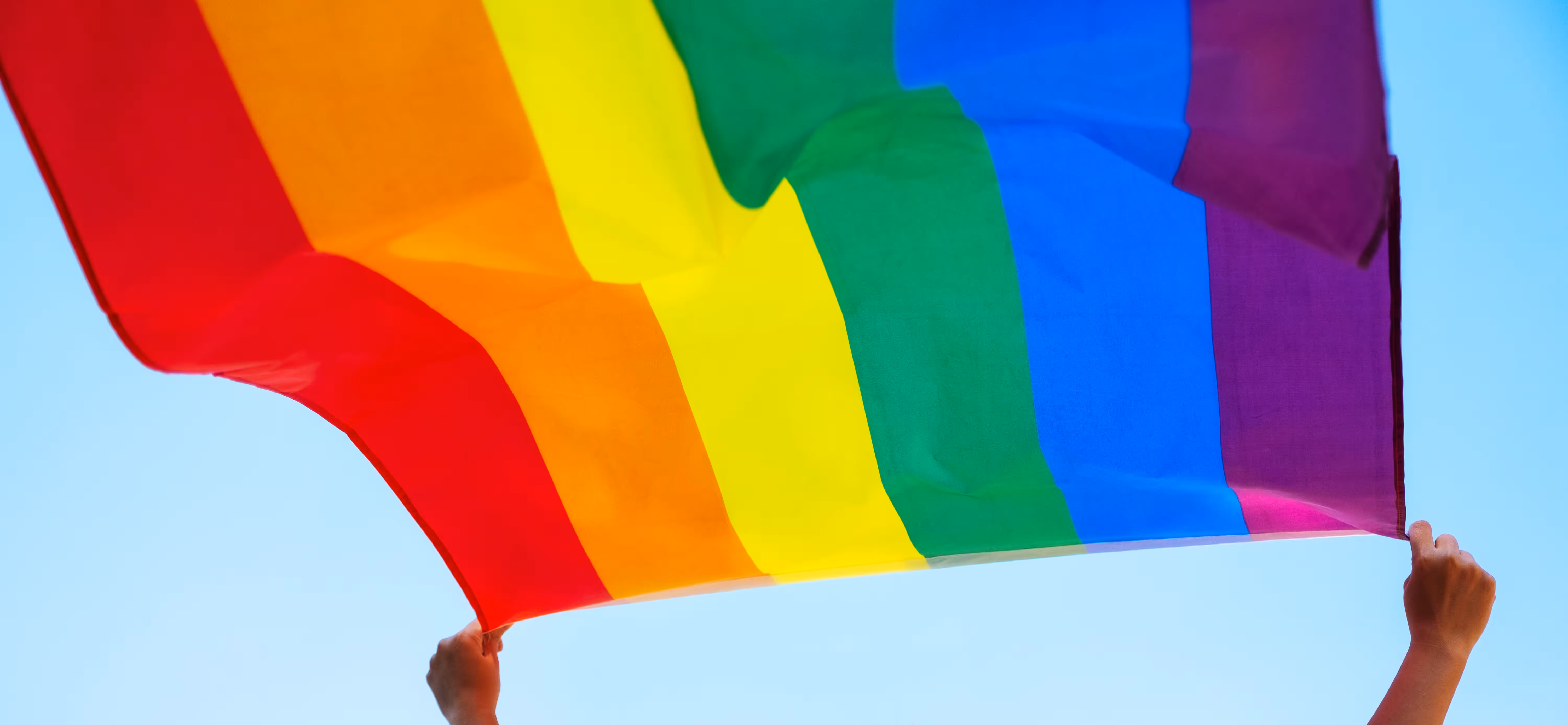 Hands holding a rainbow flag against the sky, same sex partner visa Australia