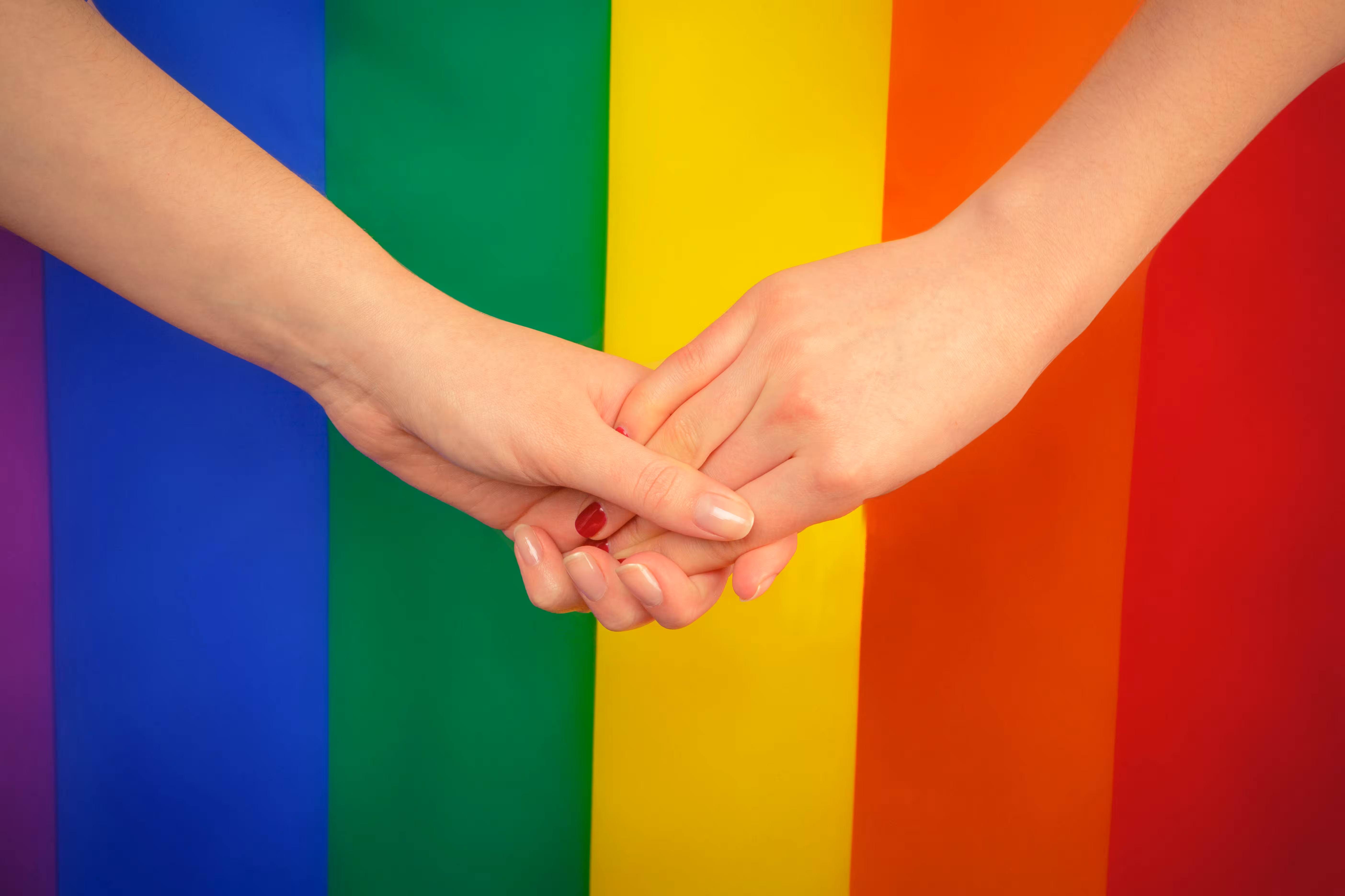 Two hands held in front of a rainbow flag, same sex partner visa Australia