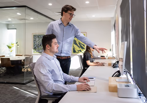 Two people reviewing brand work together at a computer in an office.