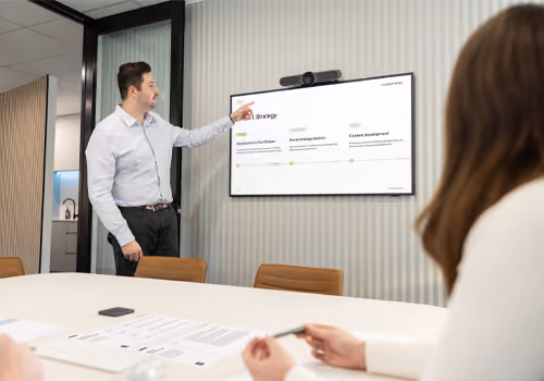 A digital strategy presentation on a wall-mounted screen, reviewed by the team from a meeting room table.