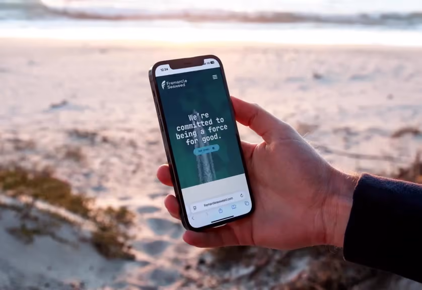 Hand holding smartphone displaying Fremantle Seaweed site with text about commitment to being a force for good.