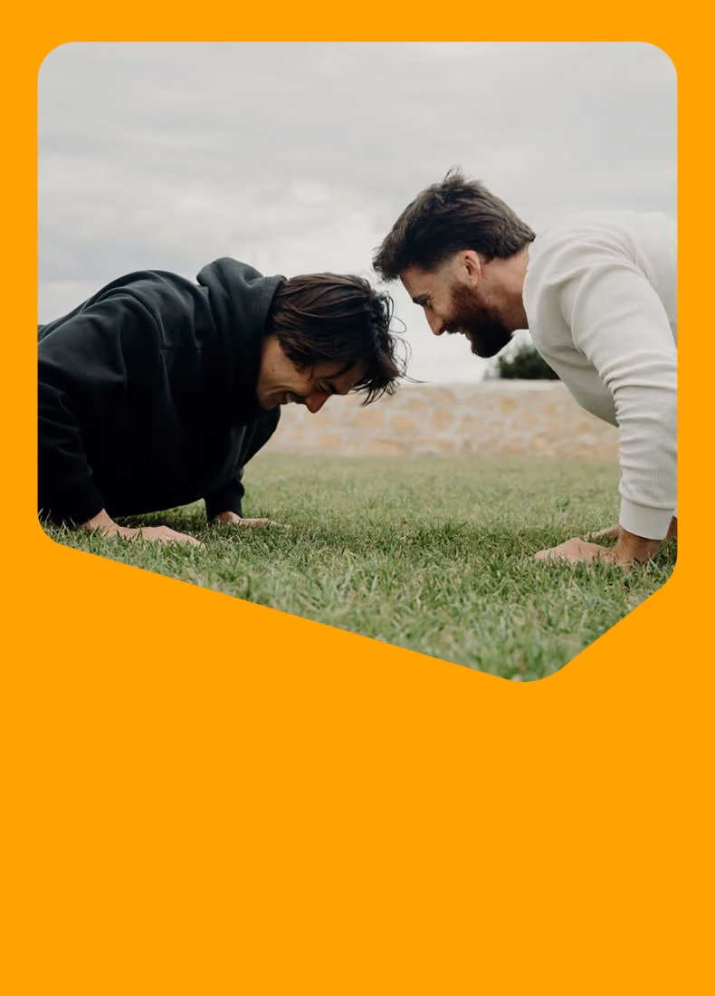 Two men doing push-ups facing each other on grass outdoors under a cloudy sky.