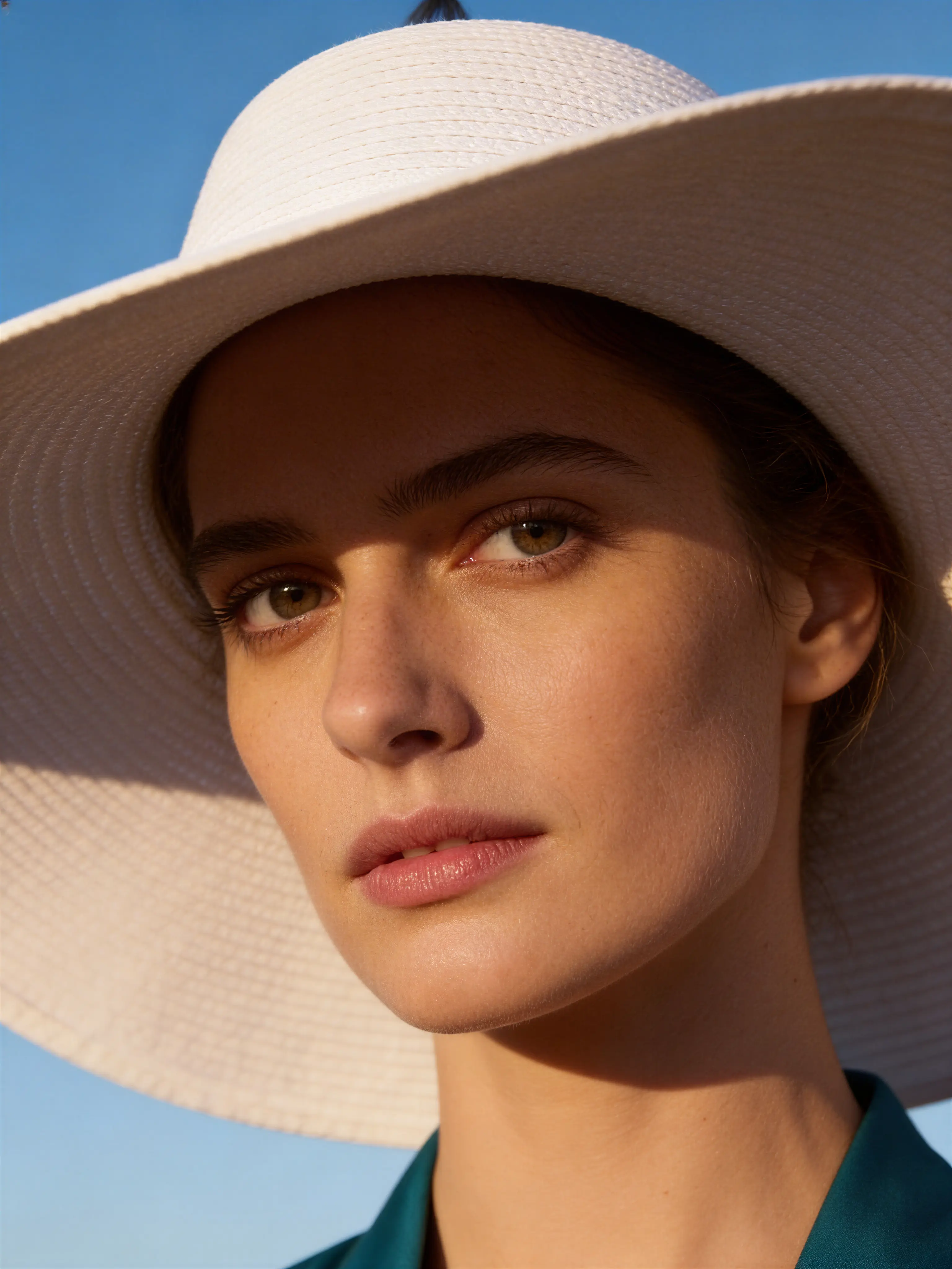Close-up of a woman wearing a wide-brimmed white hat against a blue sky.