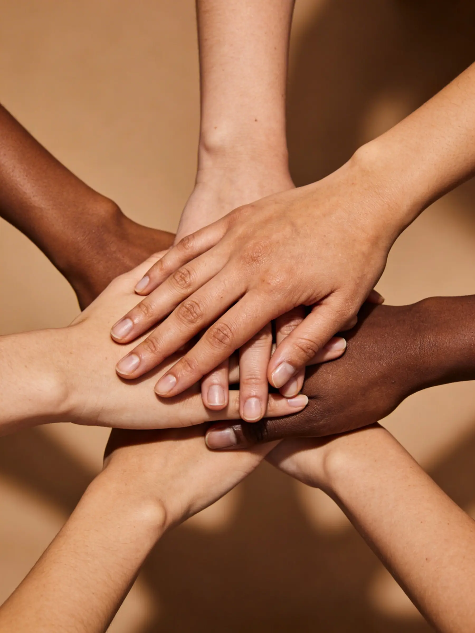 Hands of diverse skin tones stacked together symbolizing unity and teamwork.