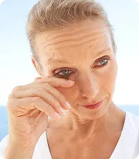 Close-up of a mature woman wiping tears from her eye in natural light.