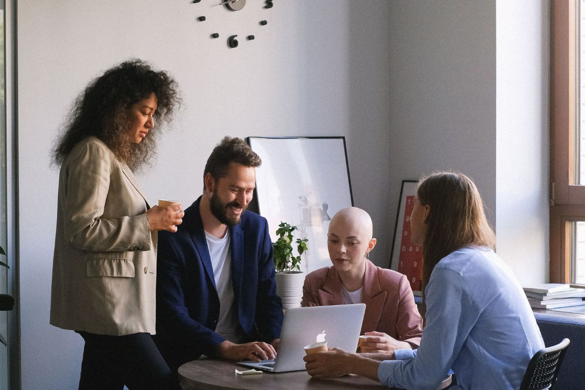 A diverse group of four office professionals gathering around a table to collaborate on a laptop, illustrating Connext Global Solutions collaborative ⁠offshore staffing and integrated team management services.