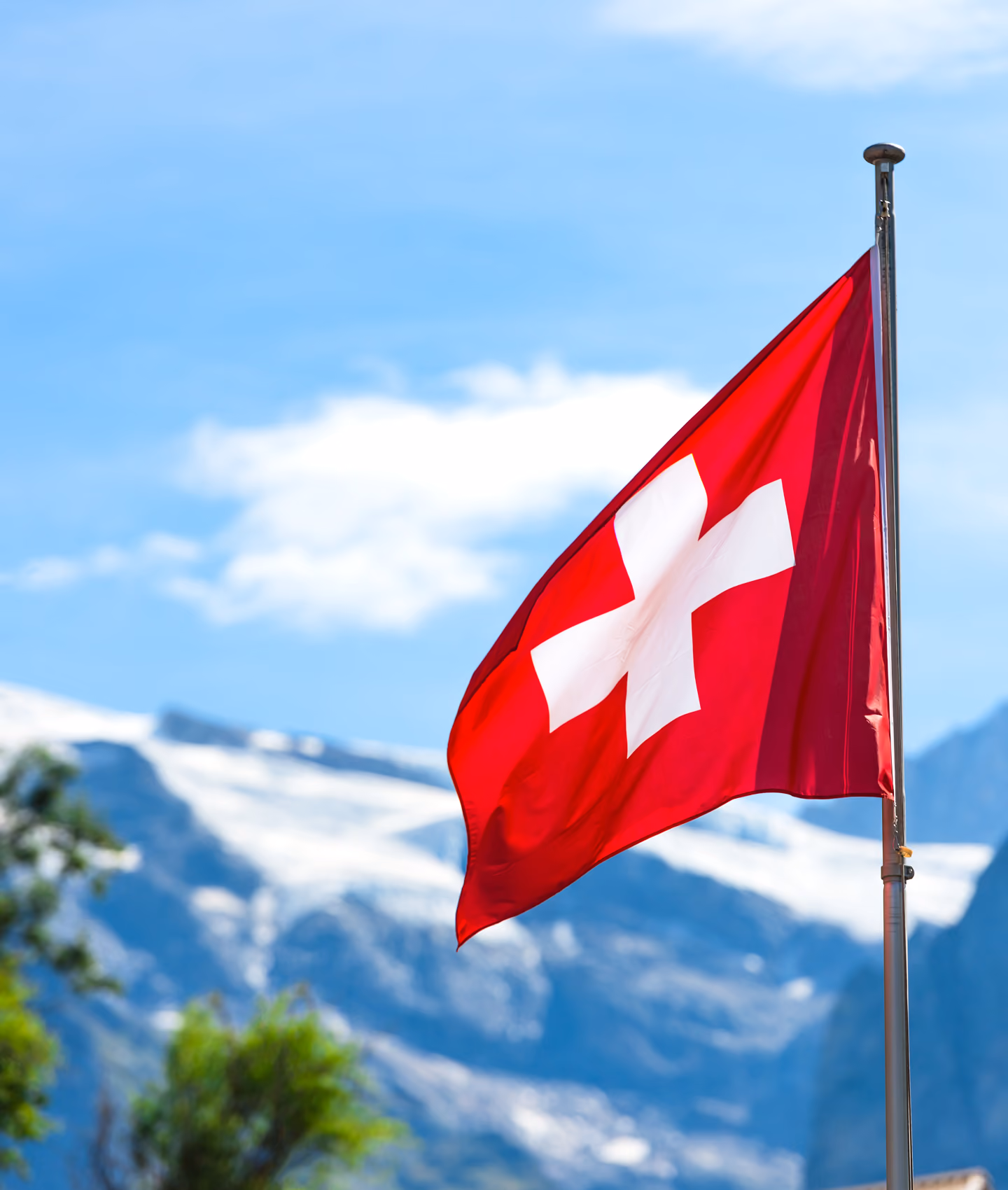 Un drapeau suisse flottant sur fond de ciel bleu clair et d'une montagne enneigée.