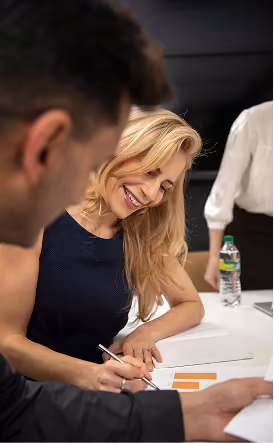 Une femme d'affaires blonde souriante écrivant sur un document financier lors d'une discussion d'équipe.