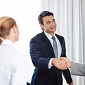 Un homme d'affaires souriant en costume sombre serrant la main d'un client dans un bureau lumineux.