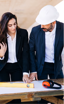 Une femme d'affaires et un ingénieur portant un casque de sécurité blanc examinent des plans d'architecture sur une table avec des outils de chantier.