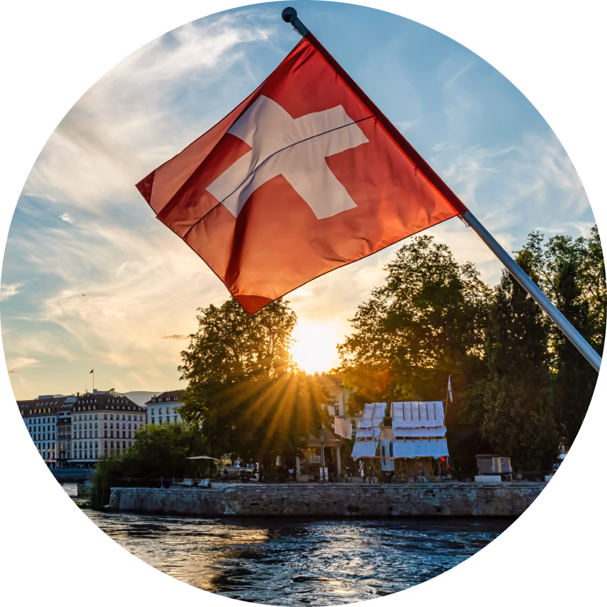 Un drapeau suisse flottant au-dessus de l'eau au coucher du soleil, avec les rayons du soleil perçant à travers les arbres sur la rive en arrière-plan.