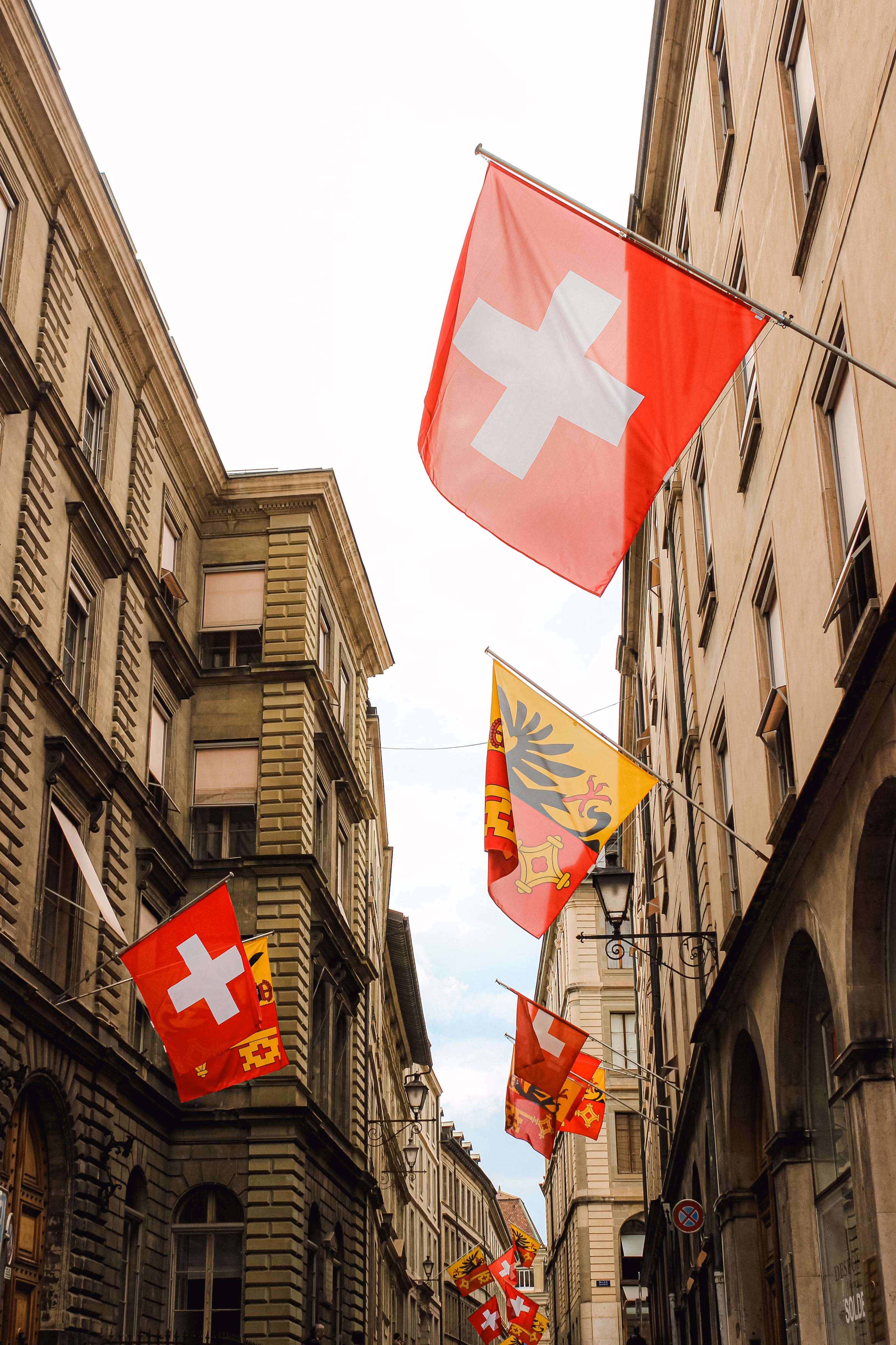 Une rue étroite bordée de bâtiments historiques en pierre à Genève, décorée de drapeaux suisses et du canton de Genève suspendus au-dessus de la rue.