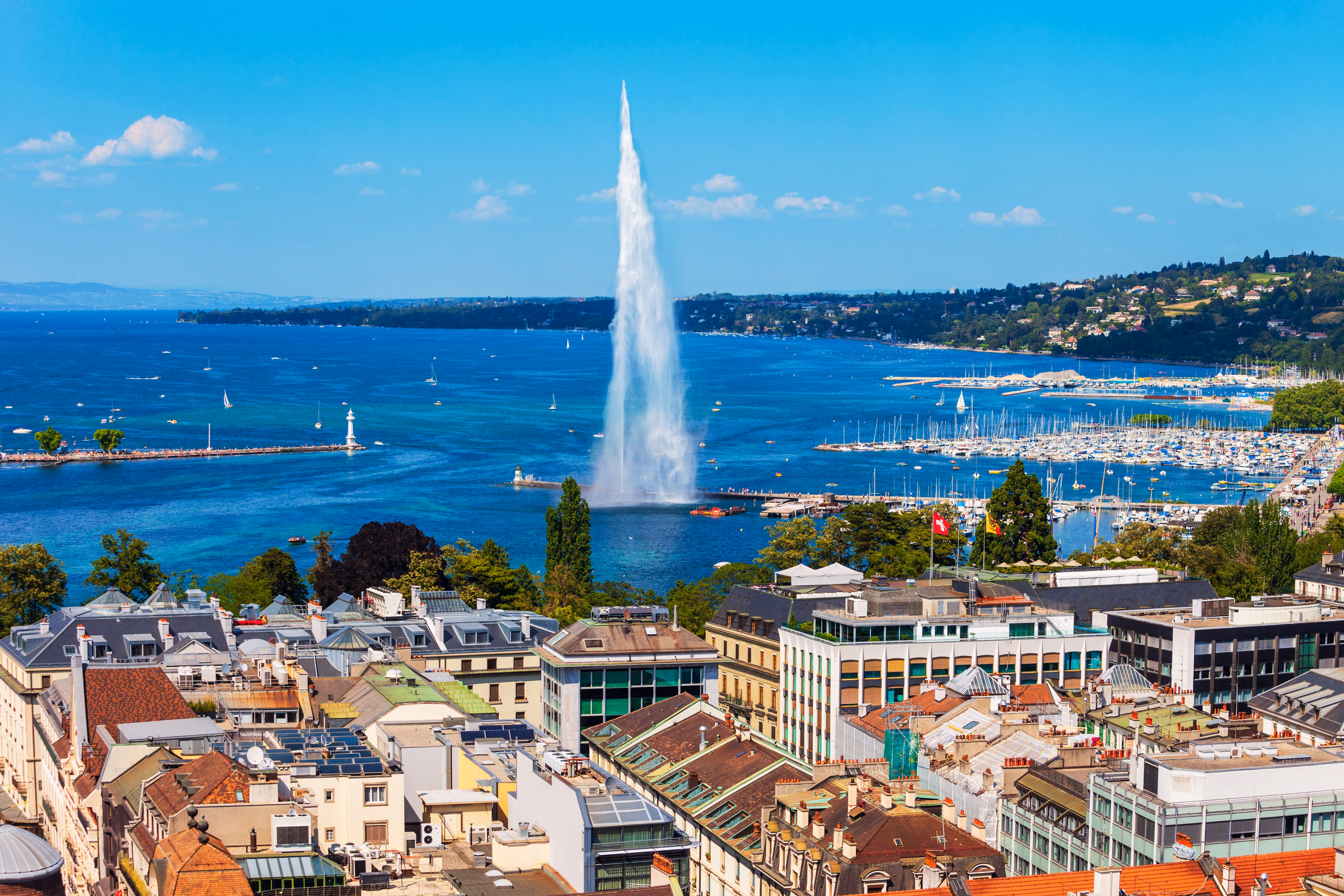 Une vue en hauteur des toits de Genève orientée vers les eaux bleu vif du lac Léman, la marina et le Jet d'Eau.