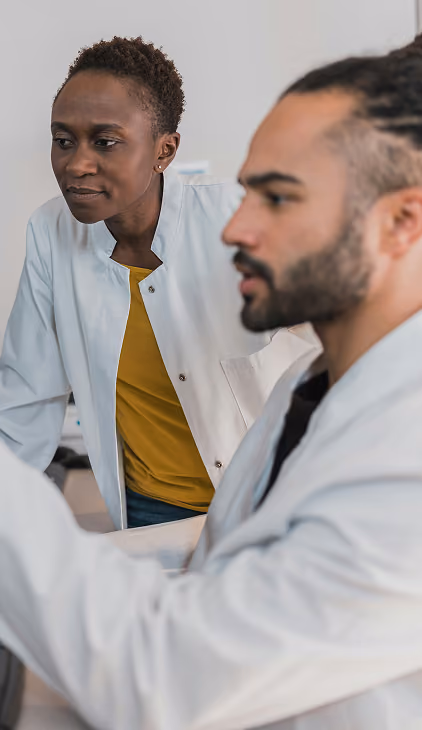 Two scientists in white lab coats working intently together in a laboratory setting.