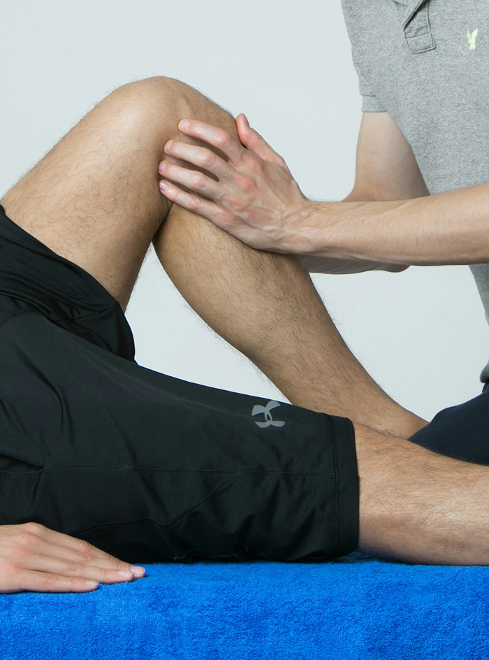 Physical therapist holding and stretching a person's bent leg while the person lies on a blue towel.