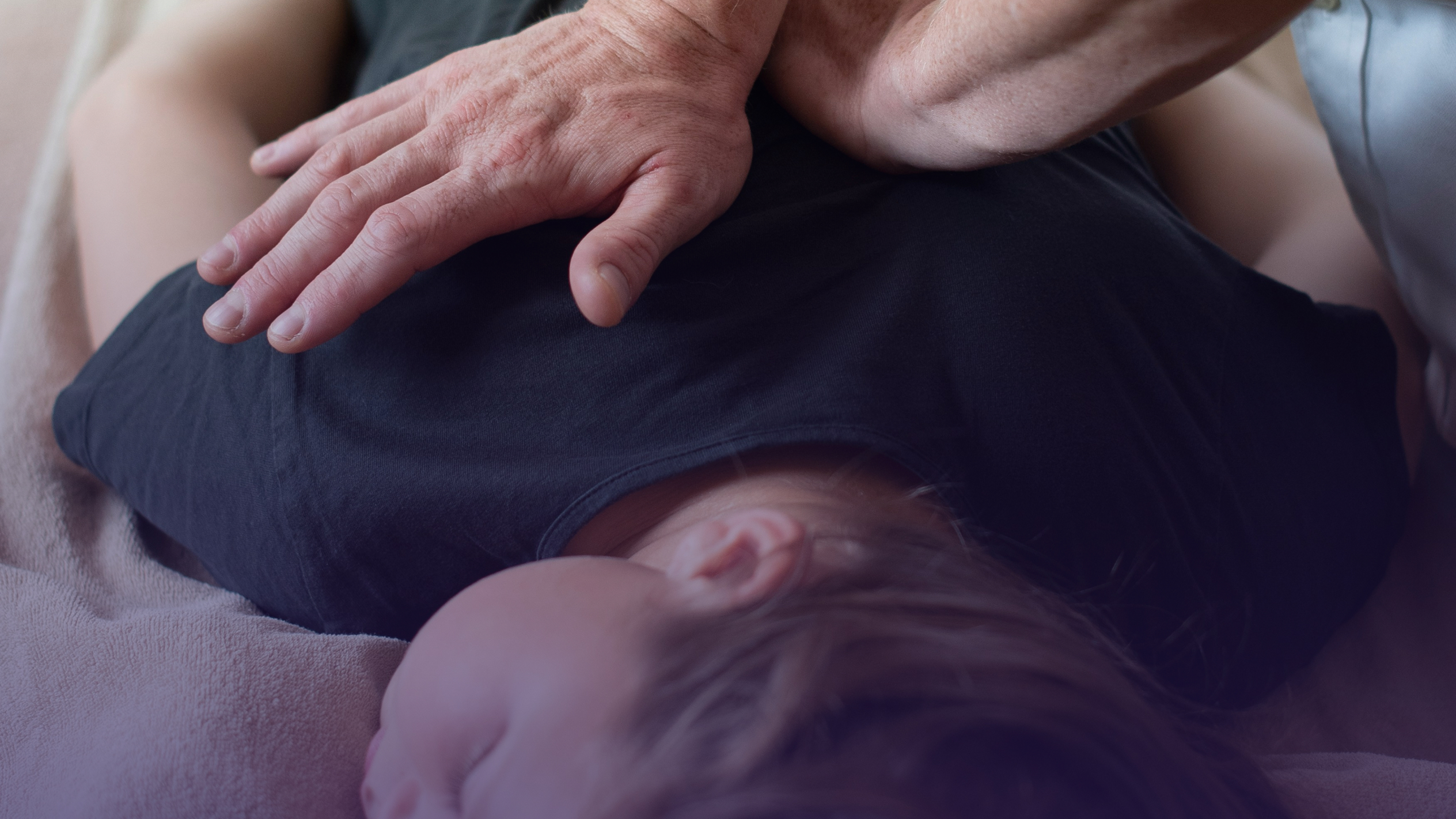 Close-up of a person lying face down on a soft surface with another person's hand gently placed on their upper back.