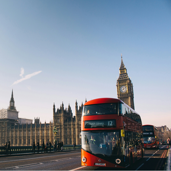 Red double-decker bus on Westminster Bridge with Big Ben and the Palace of Westminster in the background under a clear blue sky.