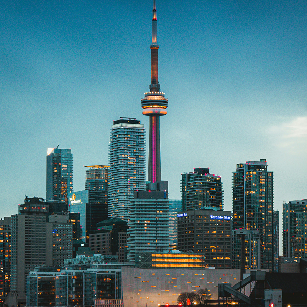 Toronto skyline at dusk with the CN Tower illuminated in purple and orange light standing prominently among modern high-rise buildings including the Toronto Star building.