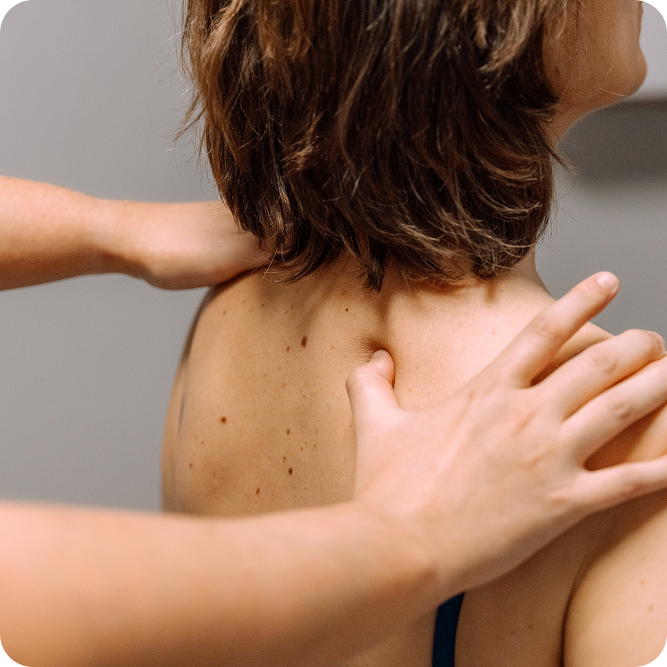 A person receiving a shoulder massage with hands pressing on their upper back near the neck.