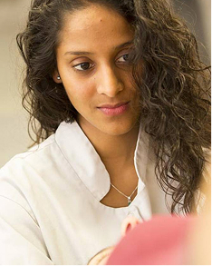 Woman with long curly hair wearing a white collared shirt, looking downward with a gentle expression.