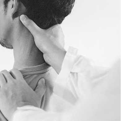 A person wearing a white coat uses their hands to examine or massage the neck and upper shoulder of another person facing away.