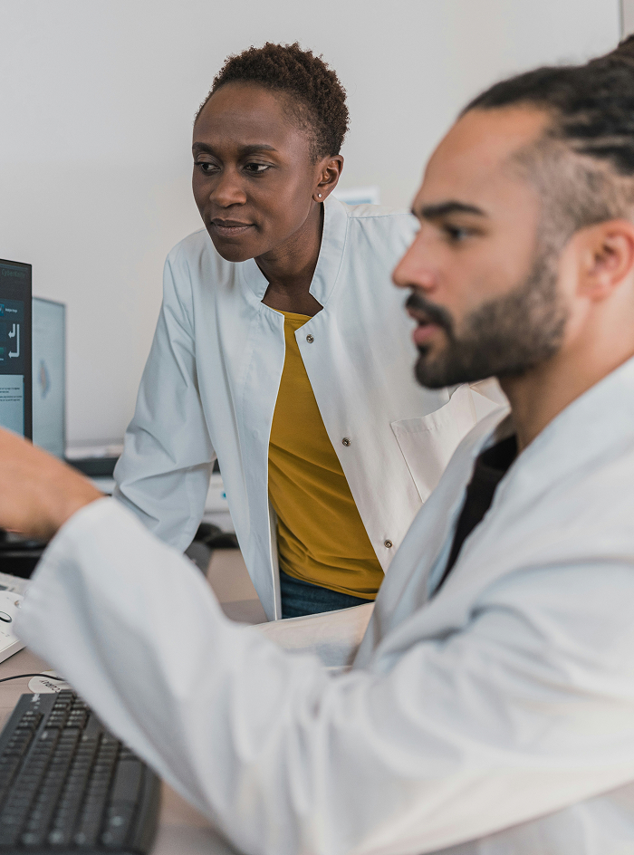 Two scientists in white lab coats looking at a computer screen, with one pointing at the screen and the other observing intently.