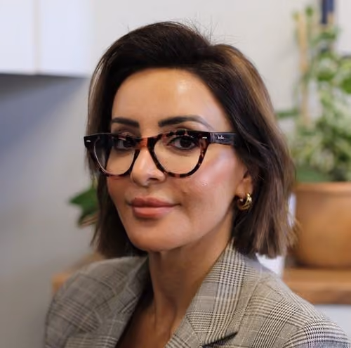 Woman with short brown hair wearing tortoiseshell glasses and a plaid blazer, smiling slightly.