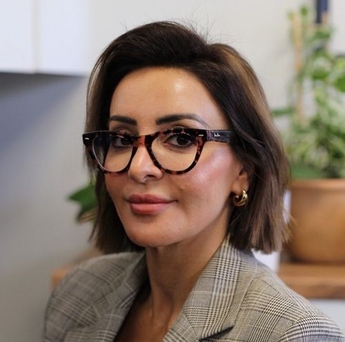 Woman with short brown hair wearing tortoiseshell glasses and a plaid blazer, smiling slightly.