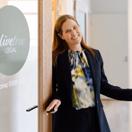 Smiling woman in business attire leaning on an office door with 'Livetree Legal' logo.
