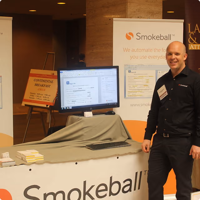 Man standing at a Smokeball booth with computer monitor displaying legal software interface.