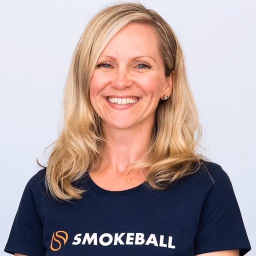 Smiling blond woman wearing a navy Smokeball t-shirt against a plain light background.
