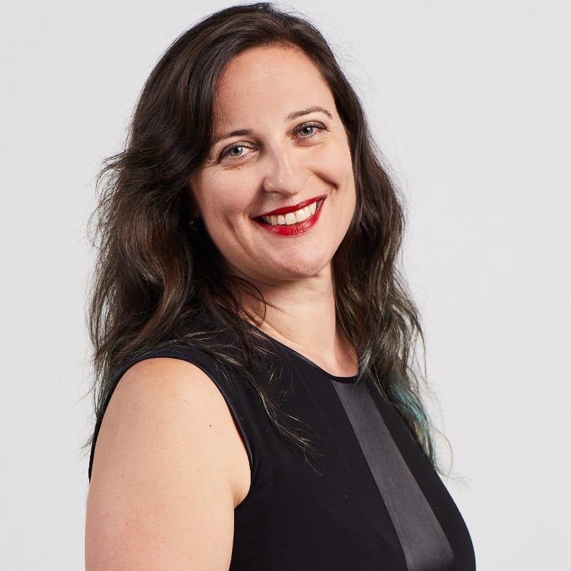Woman with long dark hair in a sleeveless black top smiling at the camera against a plain background.