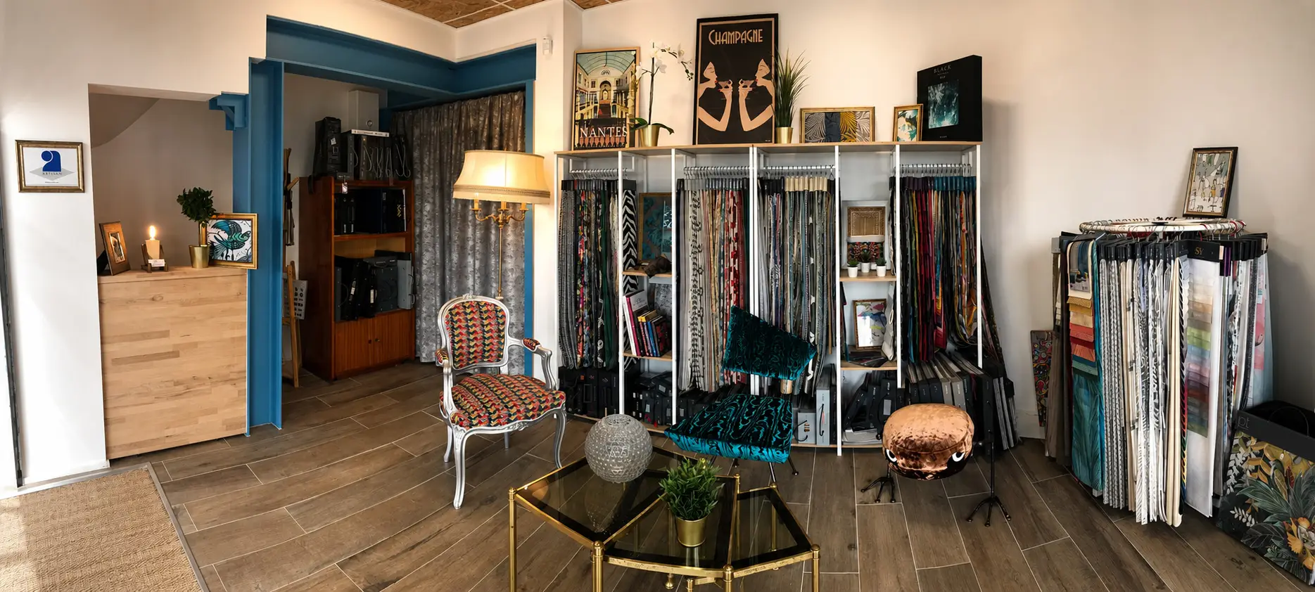 Interior of a fabric showroom with patterned chairs, sample racks, framed art, and plants.