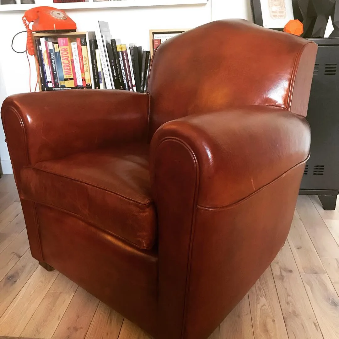 Brown leather armchair on wooden floor with bookshelf and orange rotary phone in background.